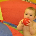 Baby mit rotem Ball auf buntem Schwungtuch sitzend